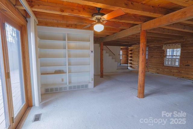 interior space with beamed ceiling, carpet flooring, rustic walls, ceiling fan, and wooden ceiling