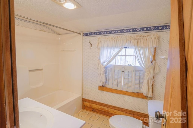 full bathroom with a sink, wallpapered walls, a textured ceiling, toilet, and shower / bathtub combination