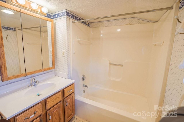 full bath with a textured ceiling, wallpapered walls, vanity, and  shower combination
