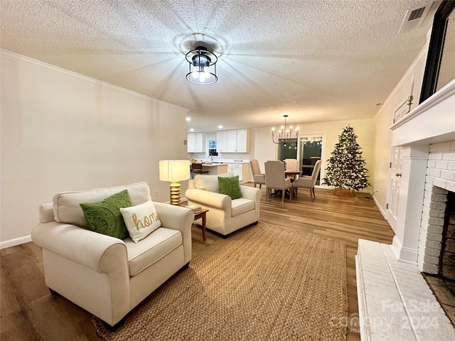 living room with a brick fireplace, a notable chandelier, crown molding, hardwood / wood-style floors, and a textured ceiling