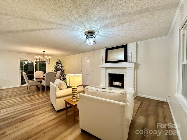 living room featuring a chandelier, wood-type flooring, a textured ceiling, a fireplace, and ornamental molding