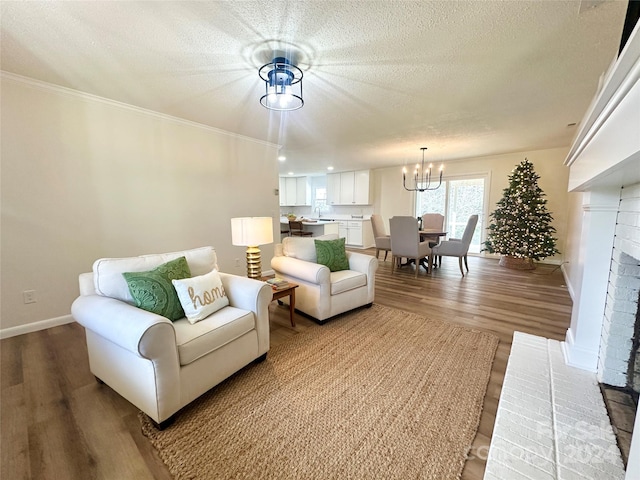 living room featuring a brick fireplace, a textured ceiling, crown molding, wood-type flooring, and a notable chandelier