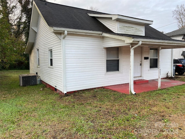 rear view of house with central air condition unit, a lawn, and a patio