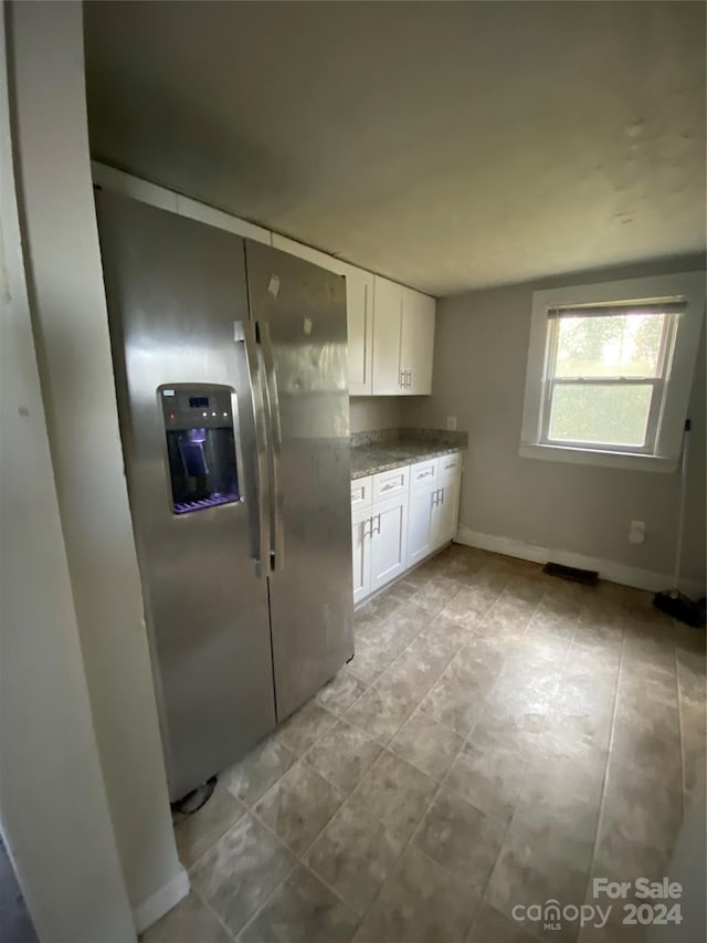 kitchen with stone counters, stainless steel fridge, and white cabinetry