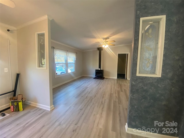 unfurnished living room with a wood stove, ceiling fan, wood-type flooring, and ornamental molding