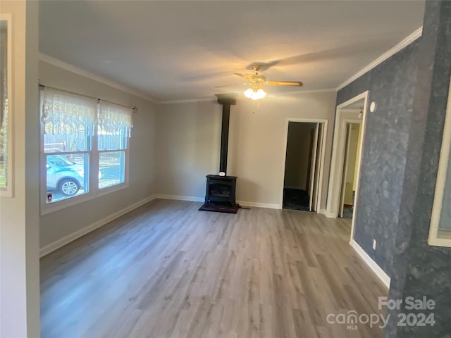 unfurnished living room featuring hardwood / wood-style flooring, ceiling fan, a wood stove, and crown molding