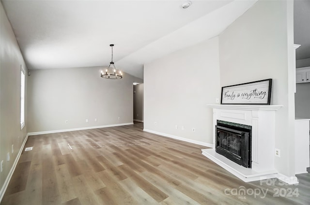 unfurnished living room featuring a high end fireplace, light hardwood / wood-style flooring, vaulted ceiling, and a chandelier