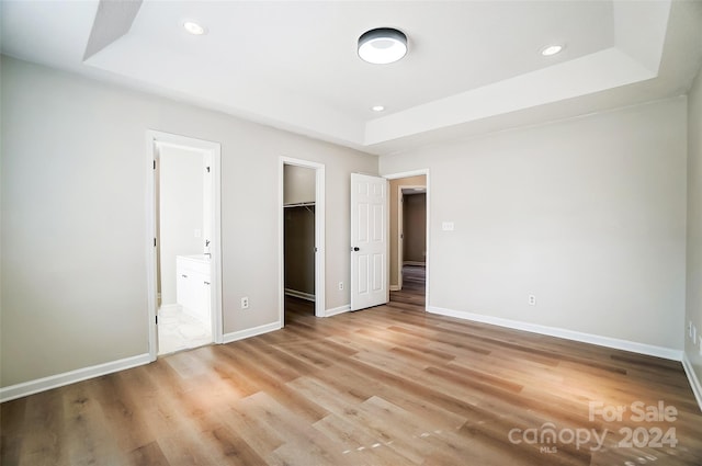 unfurnished bedroom with a raised ceiling, ensuite bath, a spacious closet, light hardwood / wood-style floors, and a closet