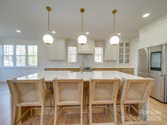 kitchen with a center island with sink, light countertops, appliances with stainless steel finishes, white cabinetry, and light wood-type flooring