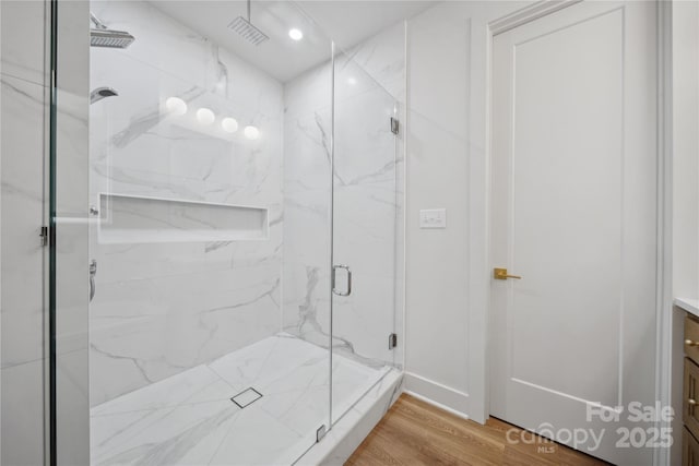 bathroom with a marble finish shower, visible vents, vanity, and wood finished floors