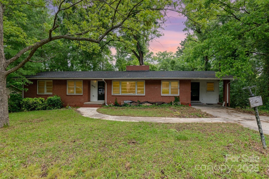 single story home featuring brick siding, concrete driveway, a lawn, and an attached carport