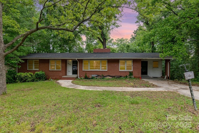 single story home featuring brick siding, concrete driveway, a lawn, and an attached carport