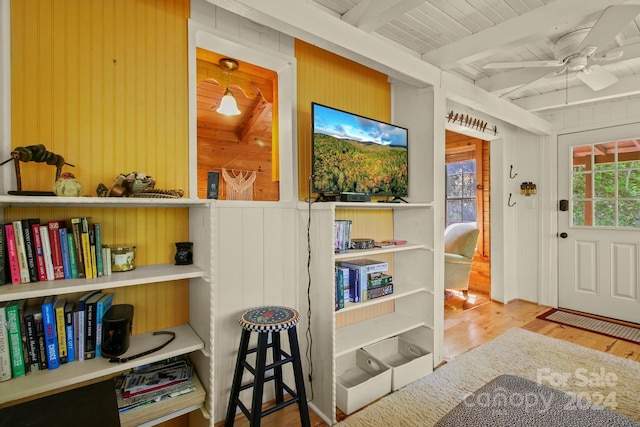 interior space with beamed ceiling, light wood-type flooring, ceiling fan, and wood walls