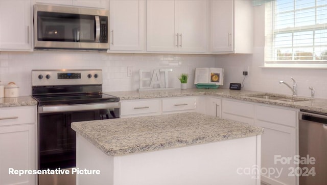 kitchen featuring white cabinets, appliances with stainless steel finishes, light stone counters, and sink