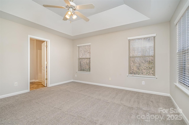 empty room with a tray ceiling, ceiling fan, and light colored carpet