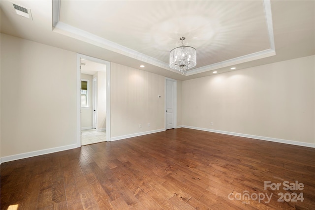 empty room featuring a raised ceiling, dark hardwood / wood-style flooring, and a notable chandelier