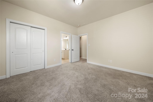 unfurnished bedroom with ensuite bathroom, a closet, and light colored carpet