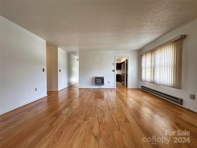 unfurnished living room with heating unit, light hardwood / wood-style flooring, a baseboard radiator, and a textured ceiling