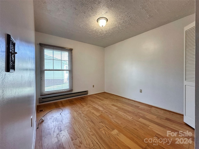 unfurnished bedroom with a textured ceiling, light wood-type flooring, and a baseboard heating unit