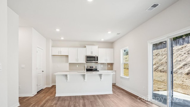 kitchen with visible vents, decorative backsplash, an island with sink, appliances with stainless steel finishes, and white cabinetry