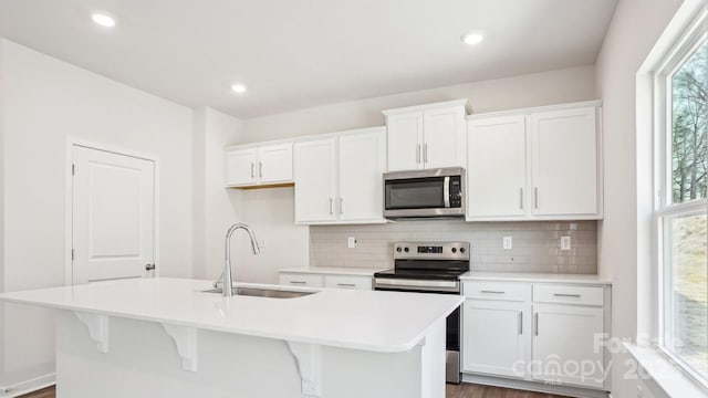 kitchen featuring stainless steel appliances, tasteful backsplash, a kitchen island with sink, white cabinets, and a sink