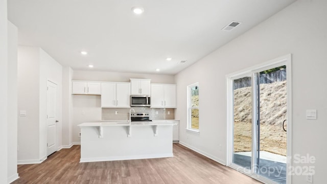 kitchen featuring visible vents, white cabinets, an island with sink, stainless steel appliances, and backsplash