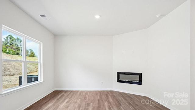 unfurnished room with a glass covered fireplace, visible vents, baseboards, and wood finished floors