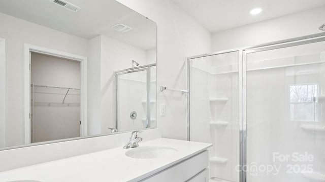 full bath featuring a walk in closet, double vanity, visible vents, a sink, and a shower stall