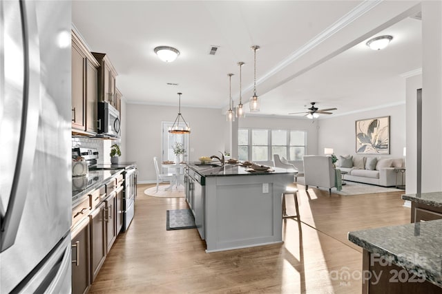 kitchen with sink, pendant lighting, a kitchen island with sink, appliances with stainless steel finishes, and light wood-type flooring