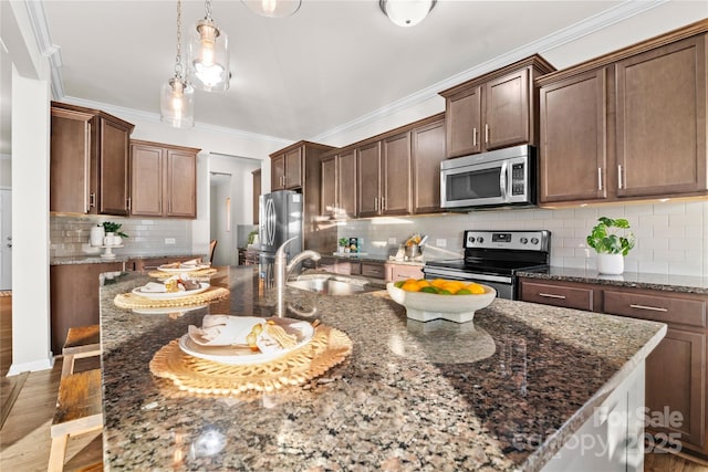 kitchen with pendant lighting, dark stone counters, a center island with sink, sink, and appliances with stainless steel finishes