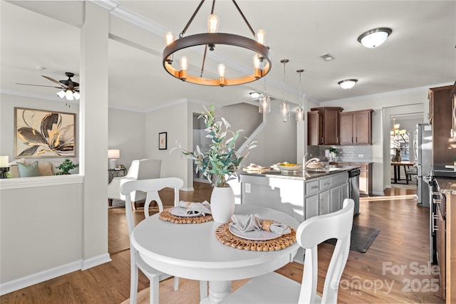 dining space with wood-type flooring, ceiling fan with notable chandelier, crown molding, and sink