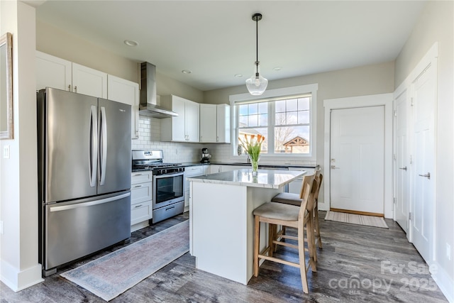 kitchen featuring pendant lighting, white cabinets, wall chimney exhaust hood, a kitchen island, and stainless steel appliances