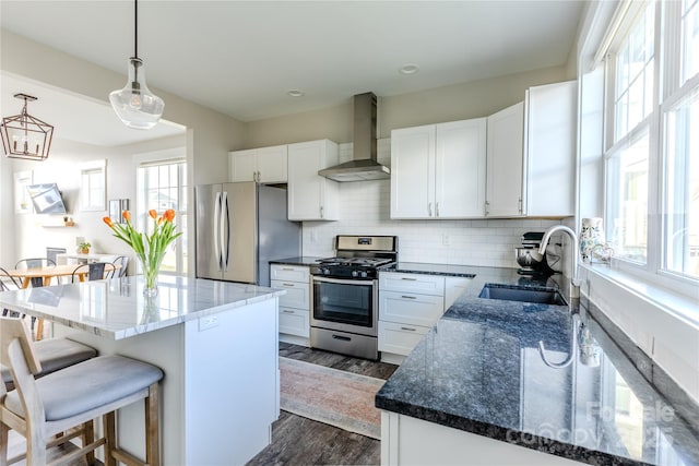 kitchen with wall chimney exhaust hood, white cabinetry, stainless steel appliances, sink, and hanging light fixtures