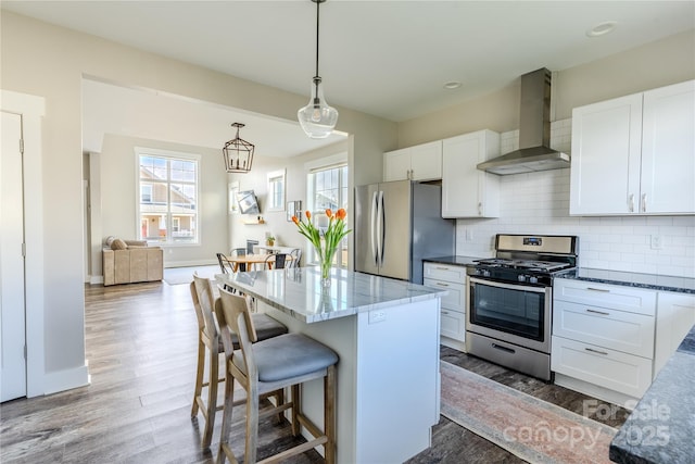 kitchen with stainless steel appliances, hanging light fixtures, wall chimney exhaust hood, white cabinets, and a center island