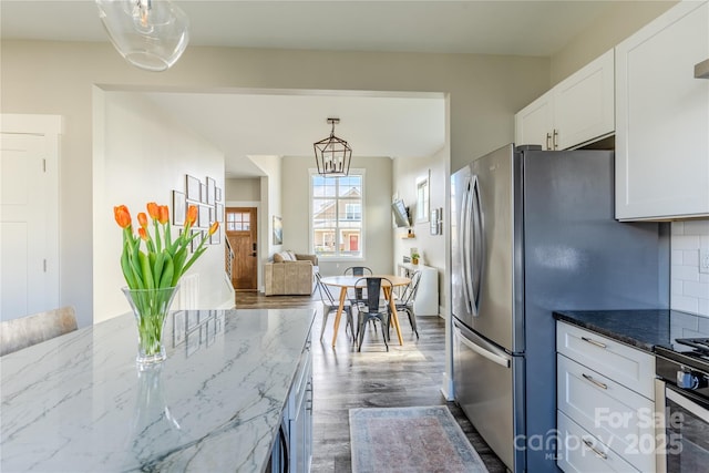 kitchen featuring white cabinets, decorative light fixtures, dark stone countertops, decorative backsplash, and stainless steel refrigerator