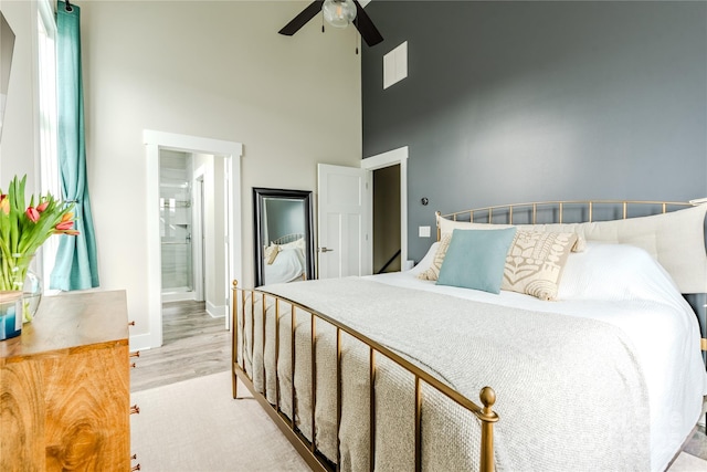 bedroom featuring ceiling fan, light hardwood / wood-style floors, a high ceiling, and ensuite bath