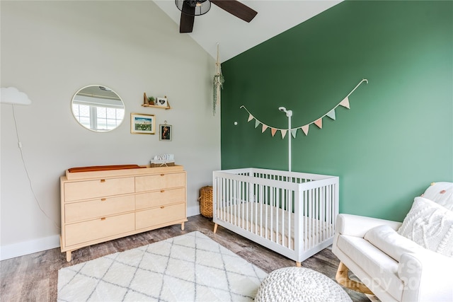 bedroom with ceiling fan, hardwood / wood-style flooring, high vaulted ceiling, and a crib