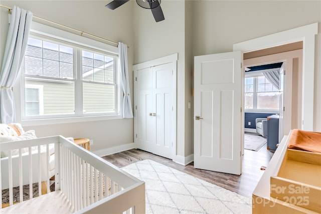 bedroom featuring ceiling fan, a nursery area, a closet, and light wood-type flooring