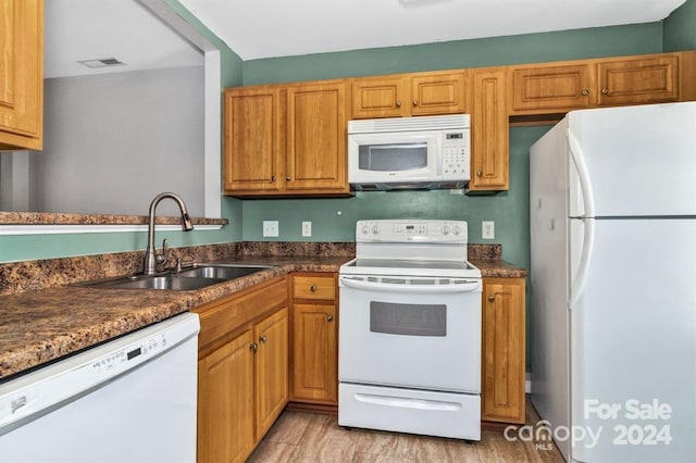 kitchen with white appliances, light hardwood / wood-style flooring, dark stone countertops, and sink