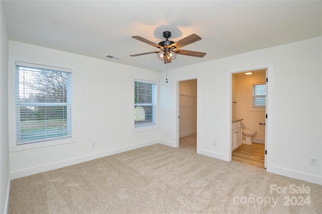 unfurnished bedroom featuring light carpet, a walk in closet, ceiling fan, connected bathroom, and a closet