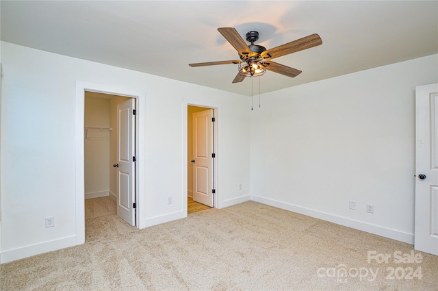 unfurnished bedroom featuring a closet, light colored carpet, a spacious closet, and ceiling fan