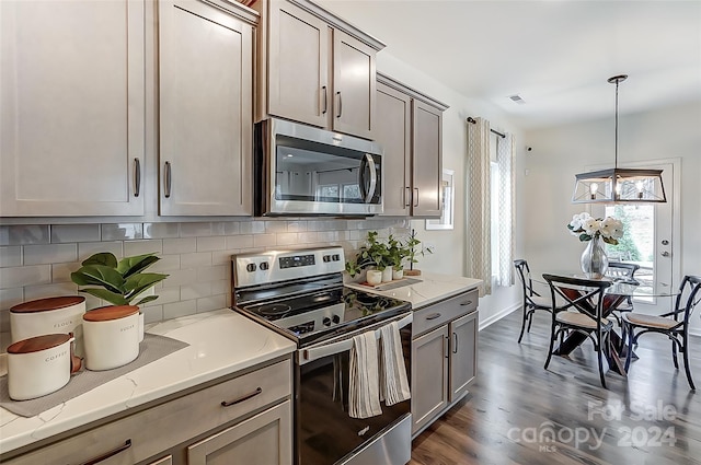 kitchen featuring light stone countertops, dark hardwood / wood-style floors, decorative light fixtures, decorative backsplash, and appliances with stainless steel finishes