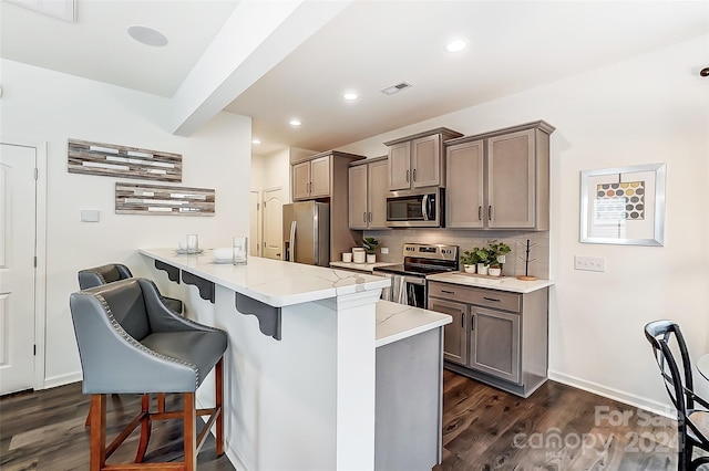 kitchen with a breakfast bar, decorative backsplash, appliances with stainless steel finishes, dark hardwood / wood-style flooring, and kitchen peninsula