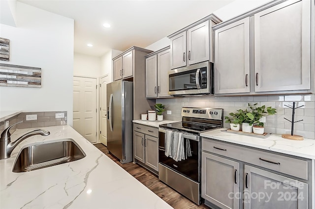 kitchen with sink, dark wood-type flooring, stainless steel appliances, light stone counters, and gray cabinets