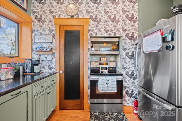 kitchen featuring dark stone counters, light wood-type flooring, appliances with stainless steel finishes, and green cabinetry