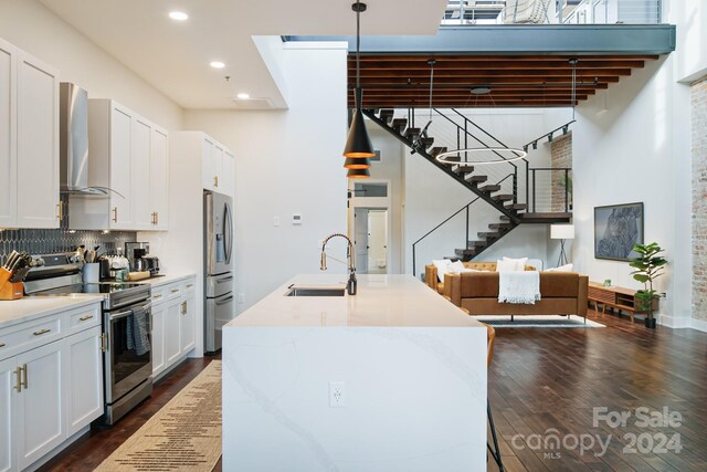 kitchen with sink, wall chimney exhaust hood, dark wood-type flooring, white cabinets, and appliances with stainless steel finishes