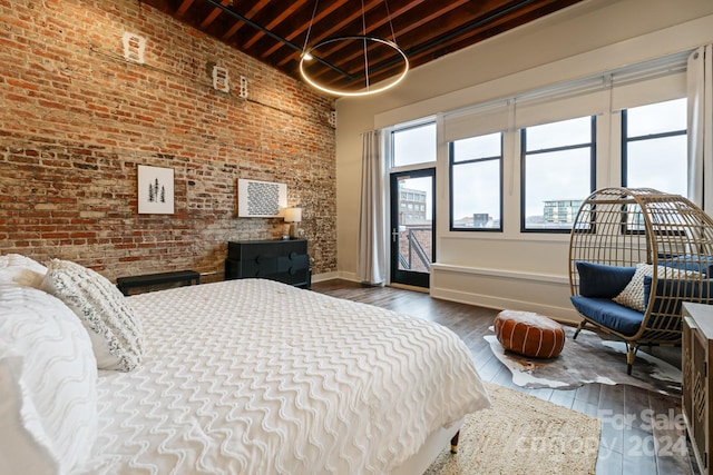 bedroom with a towering ceiling, brick wall, and dark hardwood / wood-style floors