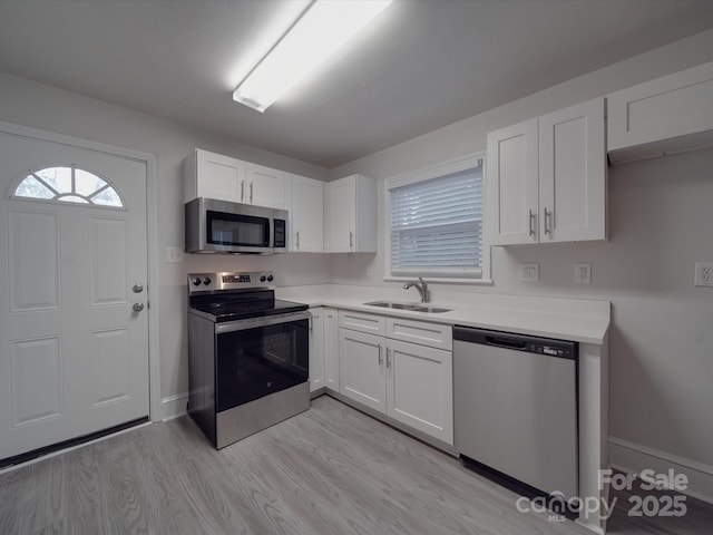 kitchen featuring stainless steel appliances, white cabinetry, sink, and light wood-type flooring