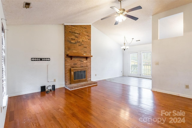 unfurnished living room featuring ceiling fan with notable chandelier, hardwood / wood-style floors, a textured ceiling, and a brick fireplace