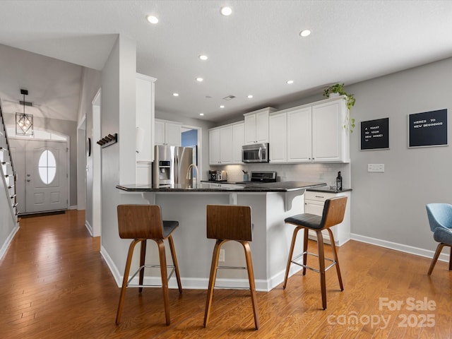 kitchen with white cabinets, decorative backsplash, appliances with stainless steel finishes, a kitchen bar, and kitchen peninsula